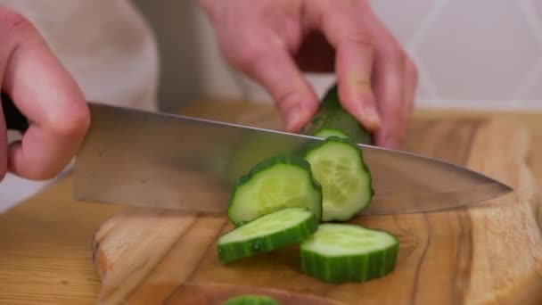 Egy férfi uborkát vág egy vágódeszkán. — Stock videók