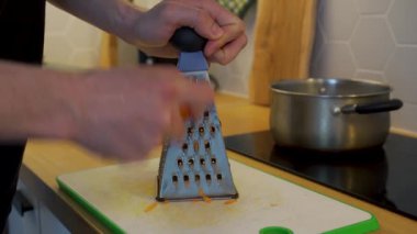 Adam mutfak masasında havuç rendeliyor.