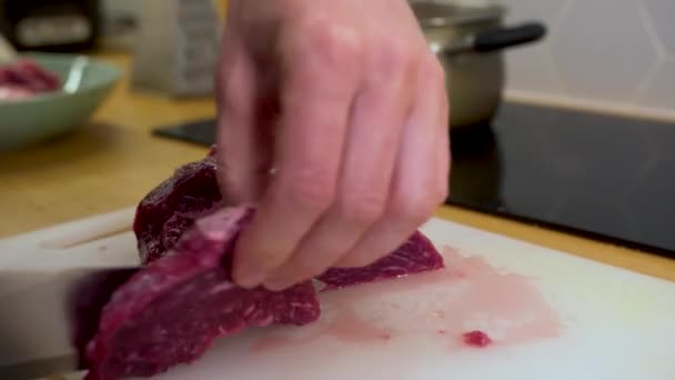 Un hombre corta un pedazo de carne, carne de res en una tabla de cortar en la cocina — Vídeos de Stock