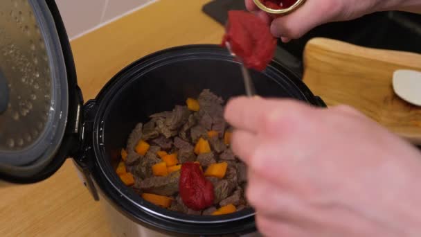Een man kookt het rundvlees in een traag fornuis, gooit een blik tomatenpuree terug — Stockvideo