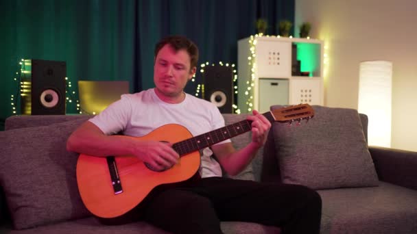 Ein Mann spielt Gitarre sitzend auf dem Sofa — Stockvideo