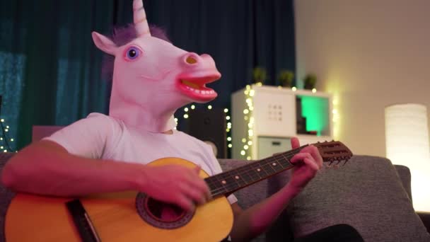 En man spelar gitarr i masken av enhörningen — Stockvideo