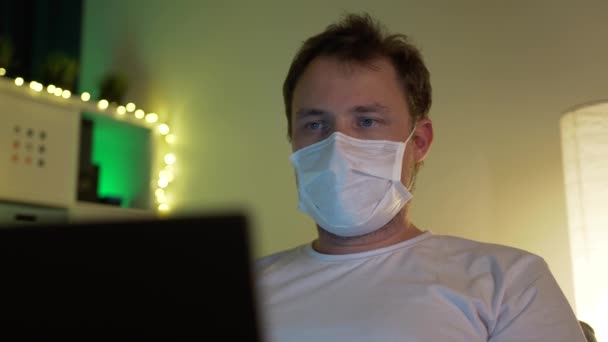 Mann mit Laptop in der Maske in heimeliger Atmosphäre — Stockvideo