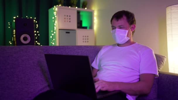 Mann mit Laptop in der Maske in heimeliger Atmosphäre — Stockvideo