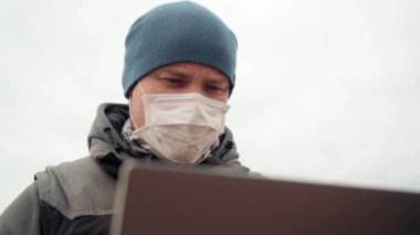 Maskeli adam. Körfezin kıyısında dizüstü bilgisayarlı bir kayanın üzerinde oturuyor.