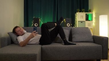 Bir adam kanepede uzanıyor, telefonuyla.