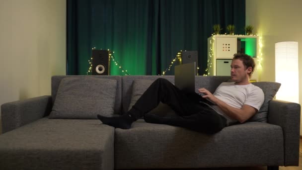 Άνθρωπος κάθεται με φορητό υπολογιστή στον καναπέ και πληκτρολογεί ένα μήνυμα — Αρχείο Βίντεο