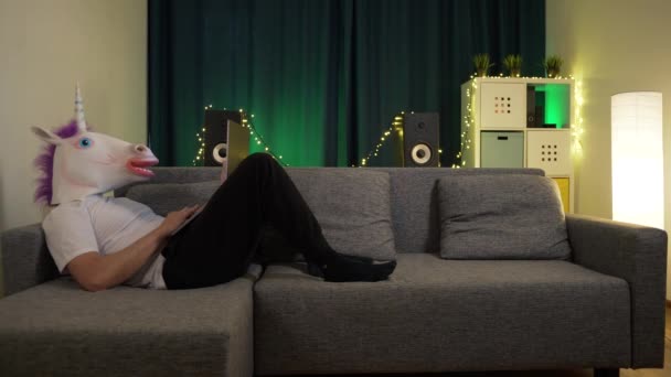 Mann in Maske sitzt mit Laptop auf Sofa und tippt eine Nachricht — Stockvideo