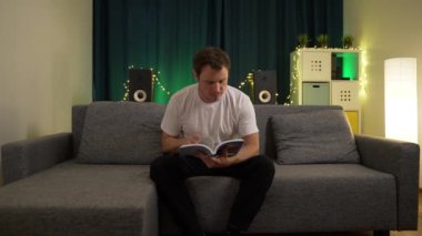 Bir adam kanepede uzanıyor ve kitap sayfalarını karıştırıyor.
