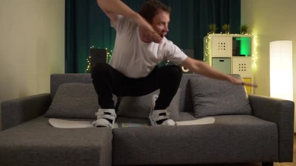 Un hombre salta sobre una tabla de snowboard en el sofá — Vídeos de Stock
