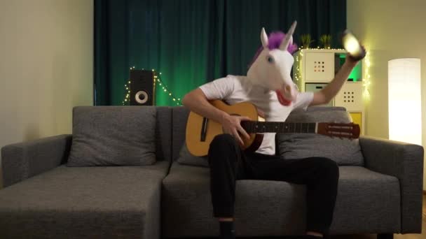 Людина в масці єдинорога грає на гітарі і танцює на музику — стокове відео