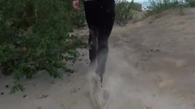 Bir adam kumda koşuyor. Arkadan gelen bir tür.