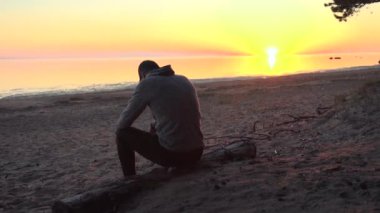 Gün batımında sahilde oturan adam.