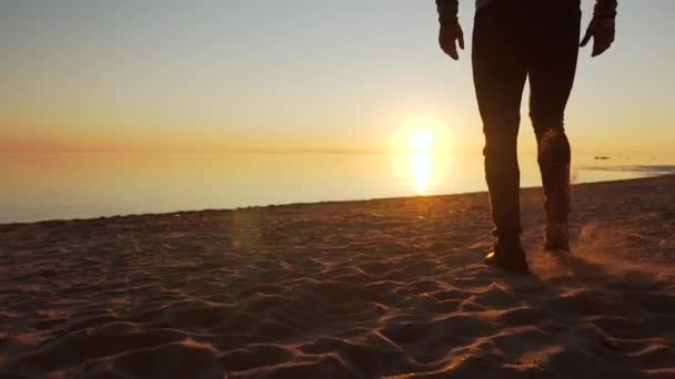 Um homem caminha ao longo da praia ao pôr do sol em frente ao mar — Vídeo de Stock