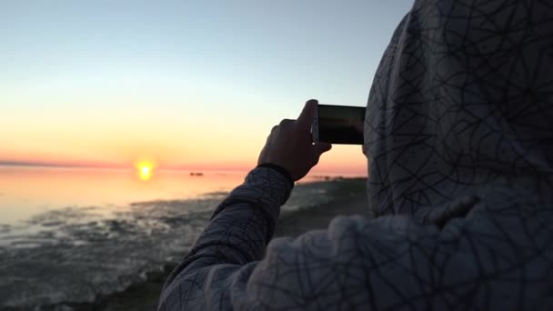 Мужчина фотографирует на смартфоне красивый закат — стоковое видео