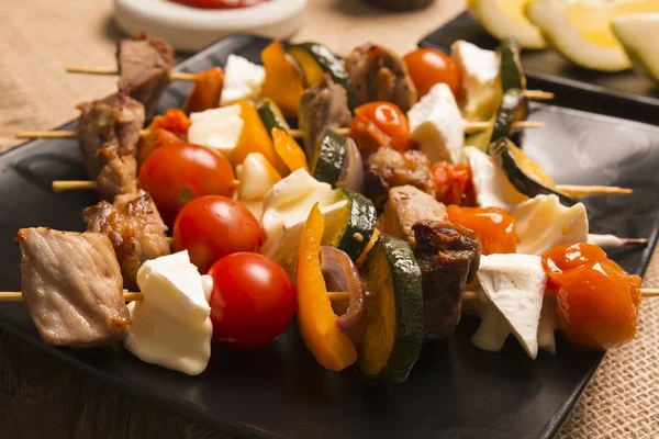 Smakfulle stekespidd med grillet kjøtt myk ost og grønnsaker servert på en mørk tallerken – stockfoto