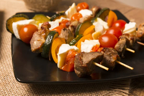 Sabrosos pinchos con carne a la parrilla de queso blando y verduras servidas en un plato oscuro —  Fotos de Stock