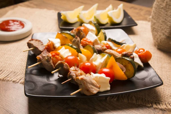 Tasty skewers with grilled meat soft cheese and vegetables served on a dark plate — Stock Photo, Image