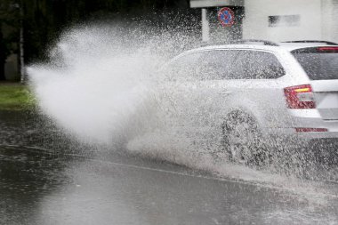 Şiddetli yağmurda sel basmış bir yolda araba sürüyor. 