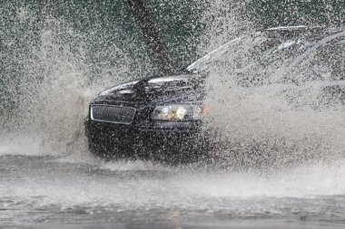 Şiddetli yağmurda sel basmış bir yolda araba sürüyor. 