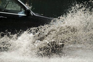 Şiddetli yağmurda sel basmış bir yolda araba sürüyor. 