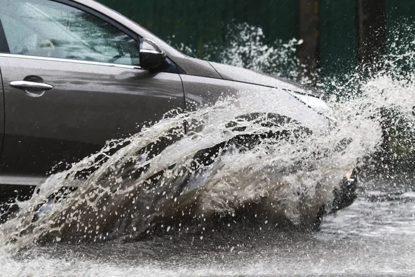 Şiddetli yağmurda sel basmış bir yolda araba sürüyor. 