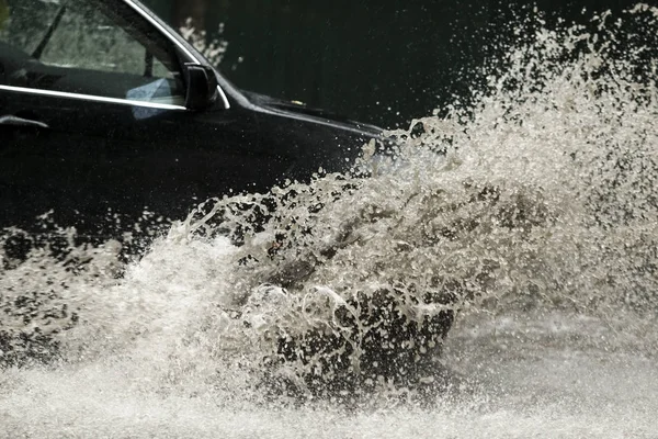 Şiddetli yağmurda sel basmış bir yolda araba sürüyor. 