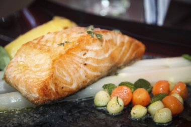 Kuşkonmaz ve sebzelerle süslenmiş ızgara somon bifteği.