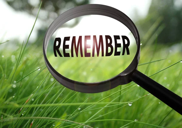 Magnifying glass with the word remember on grass background. Selective focus — Stock Photo, Image