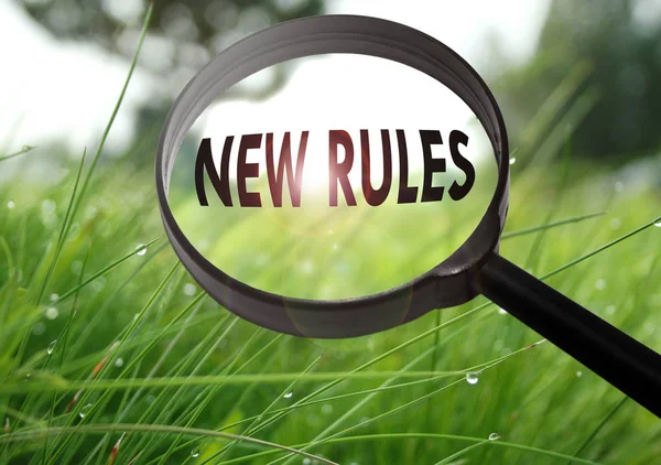 Magnifying glass with the word new rules on grass background. Selective focus — Stock Photo, Image