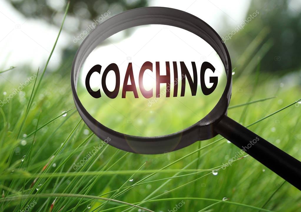 Magnifying glass with the word coaching on grass background. Selective focus