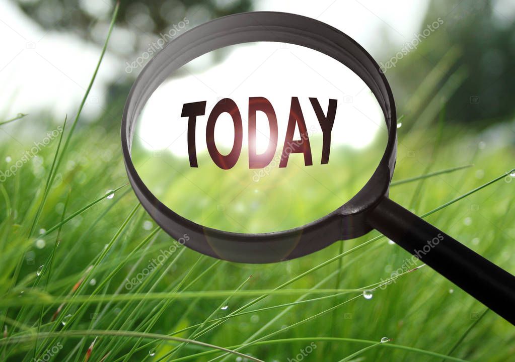 Magnifying glass with the word today on grass background. Selective focus