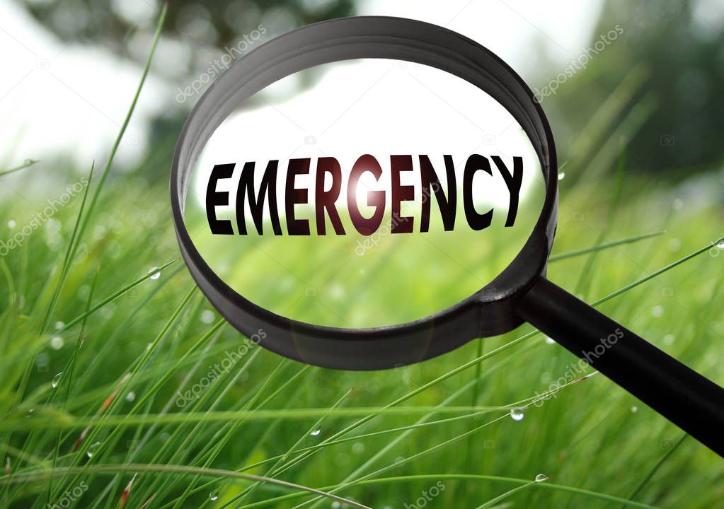 Magnifying glass with the word emergency on grass background. Selective focus