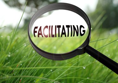 Magnifying glass with the word facilitating on grass background. Selective focus clipart
