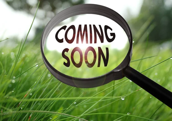 Magnifying glass with the word coming soon on grass background. Selective focus