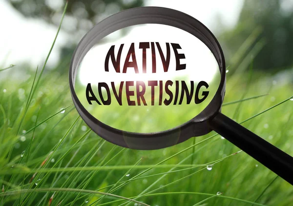 Lente d'ingrandimento con la parola pubblicità nativa su sfondo erba. Focus selettivo — Foto Stock