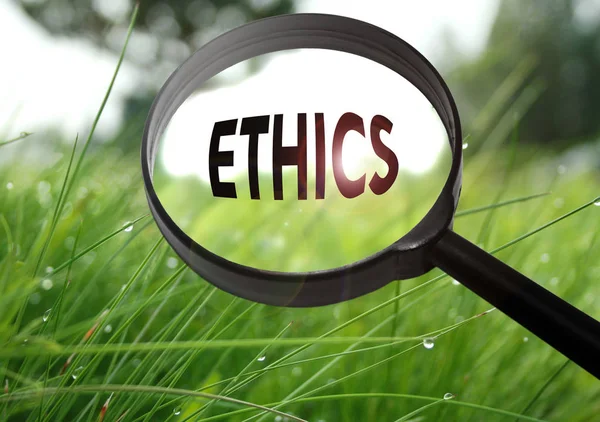 Увеличительное стекло со словом "этика" на фоне травы. Селективный фокус — стоковое фото