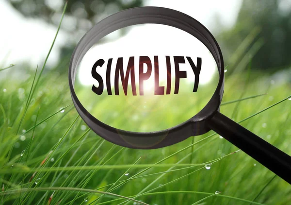 Magnifying glass with the word simplify on grass background. Selective focus — Stock Photo, Image