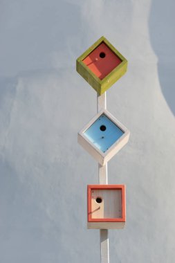 Güneşli bir günde beyaz gölgeli duvarda birbirine bağlı üç yeni modern ahşap yuva kutusu. Metin için yeri var. Resmi kapat.