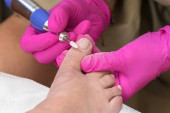 Der Pediküre-Prozess. Fußpflegerin entfernt alten Gel-Lack von Nägeln auf Zehen mit elektrischem Nagelbohrer. Weibliche Hände mit speziellen rosa Gummihandschuhen. Nahaufnahme, Draufsicht. Das Konzept von Schönheit und Gesundheit