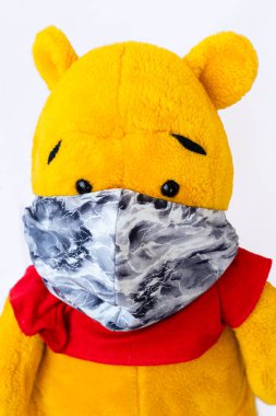 Beyaz arka planda el yapımı koruyucu maskeli sarı bir oyuncak ayı. Piyasada koruyucu ekipman eksikliği olduğu için evde bir maske yapılır. COVID-19 kavramı