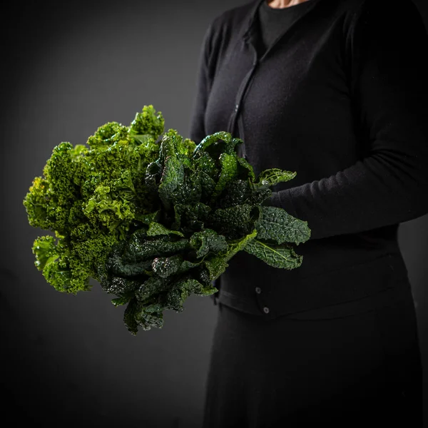 黒の女性はケール製の緑の花束を保持する 背景は黒 選択的焦点 — ストック写真