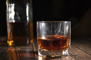Bir bardak buzlu viski, ahşap bir masada bir şişe. Işıklı eski bir masa üstü ve bir bardak sert içki..