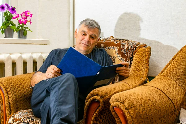 Bir adam son haberleri ya da belgeleri okuyor, belgeleri ya da faturaları kontrol ediyor, dizüstü bilgisayar kullanan, belge hazırlayan ya da oturma odasındaki koltukta otururken iletişim kuran mutlu bir adam.