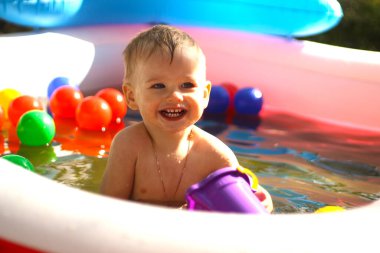 Çocuk havuzunda gülen çocuk. Güneşli yaz manzarası. Neşeli bir çocuk havuzda oynuyor. Parlak gün ışığı altında bir damla suyla..