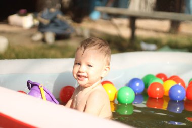 Çocuk havuzunda gülen çocuk. Güneşli yaz manzarası. Neşeli bir çocuk havuzda oynuyor. Parlak gün ışığı altında bir damla suyla..