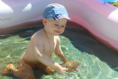 Çocuk havuzunda gülen çocuk. Güneşli yaz manzarası. Neşeli bir çocuk havuzda oynuyor. Parlak gün ışığı altında bir damla suyla..
