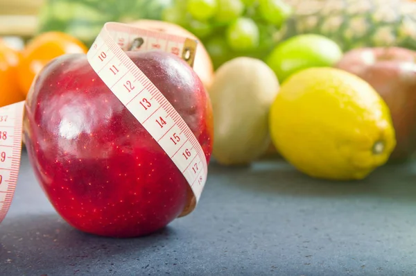 Apfel und Maßband vor fruchtigem Hintergrund — Stockfoto