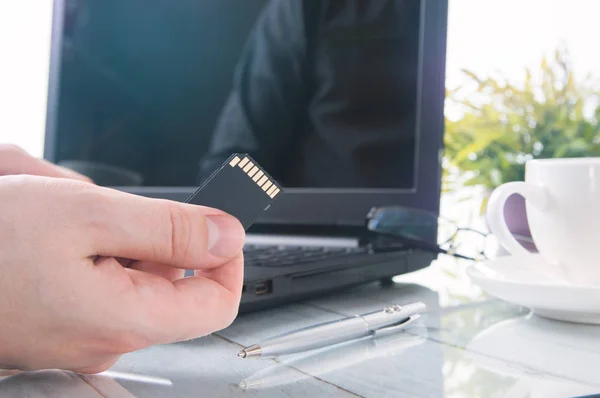 A mão do homem está segurando cartão SD contra laptop — Fotografia de Stock