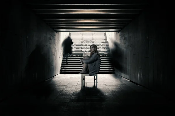 Young woman alone in a tunnel and strangers pass beyond. — Stock Photo, Image